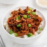 Shredded honey chicken and rice in white bowl on marble counter..