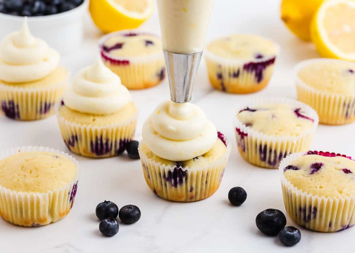 Piping lemon cream cheese frosting onto lemon blueberry cupcakes.
