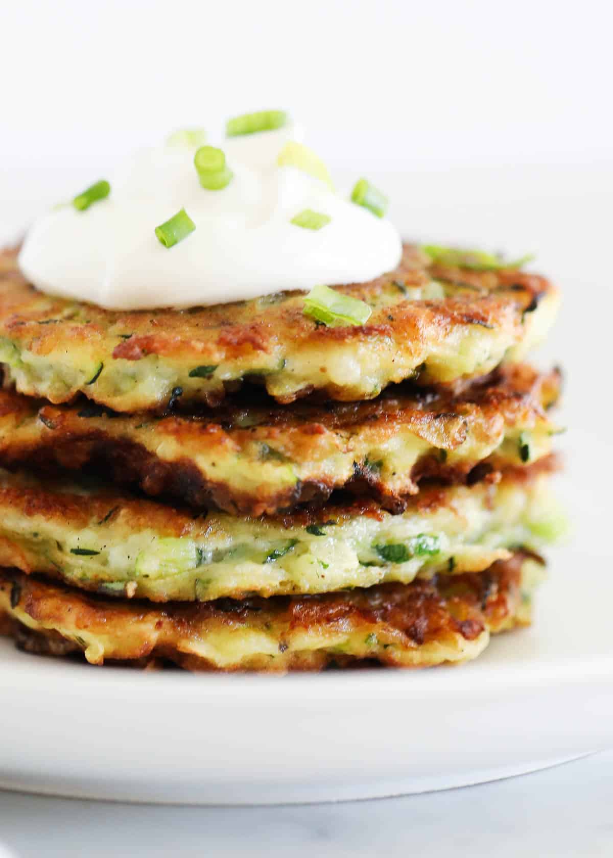 Stack of zucchini fritters on a white plate.