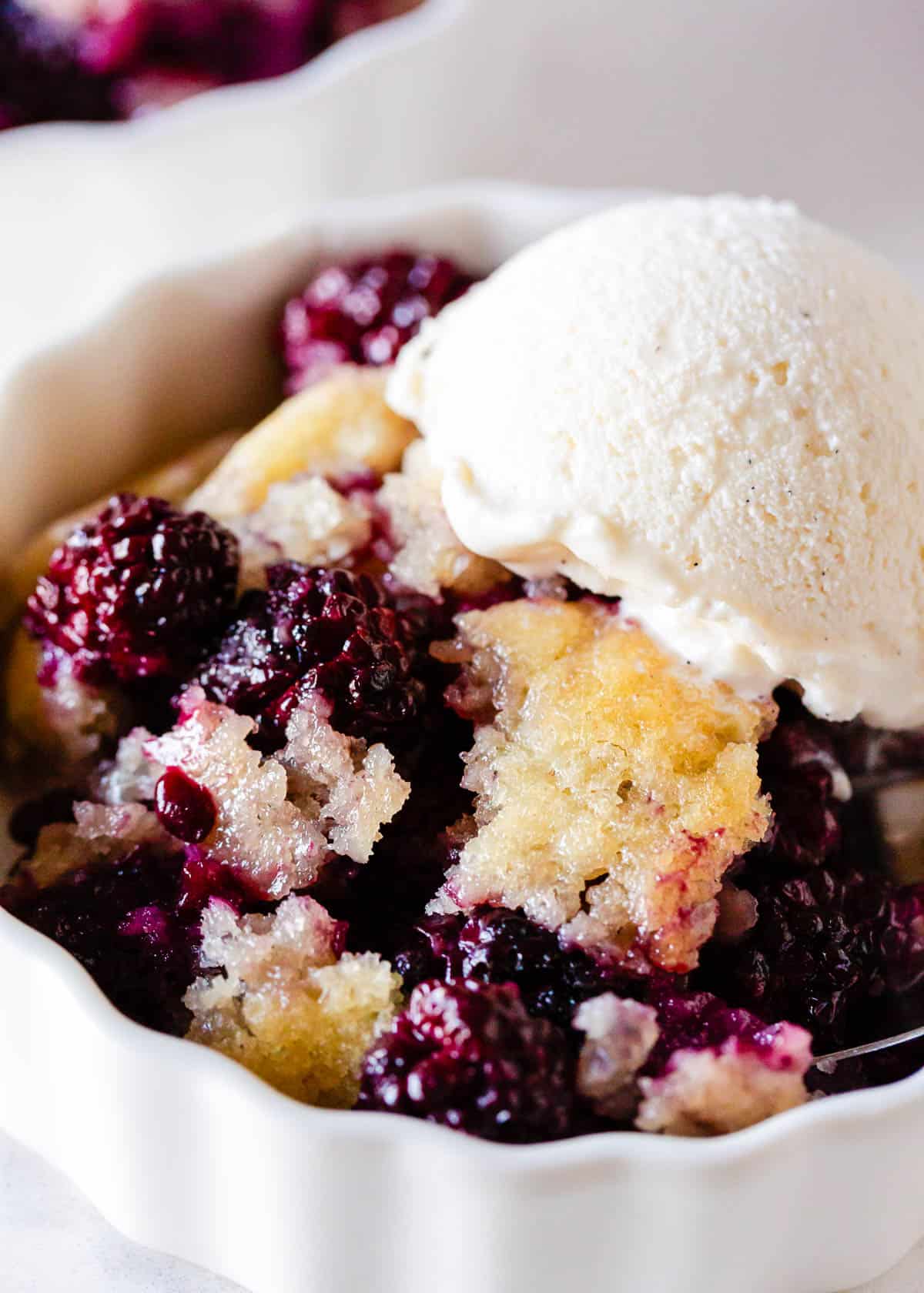 This blackberry cobbler is a classic old-fashioned dessert made with a juicy blackberry filling and a crisp, buttery, golden crust. Serve this easy sweet treat with a scoop of ice cream! Blackberry cobbler in a bowl with ice cream.