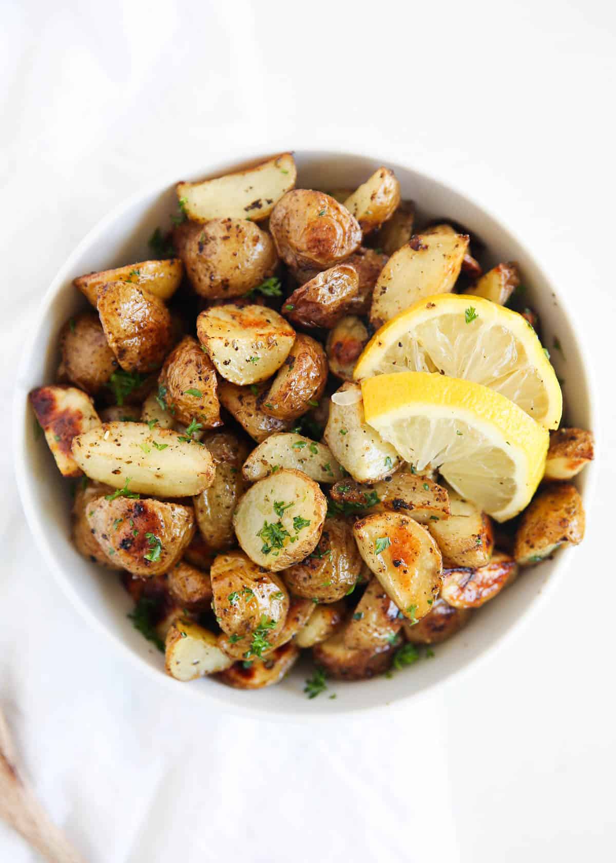 Greek potatoes in a white bowl topped with lemon slices.