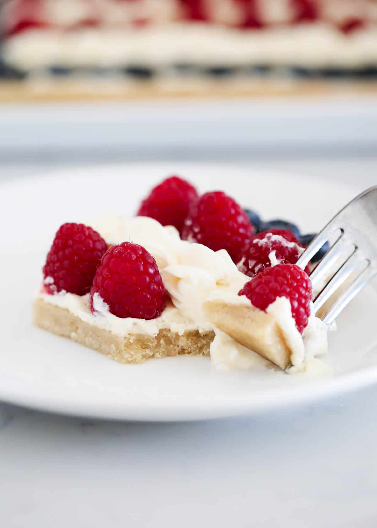 Bite taken from fruit pizza on white plate.