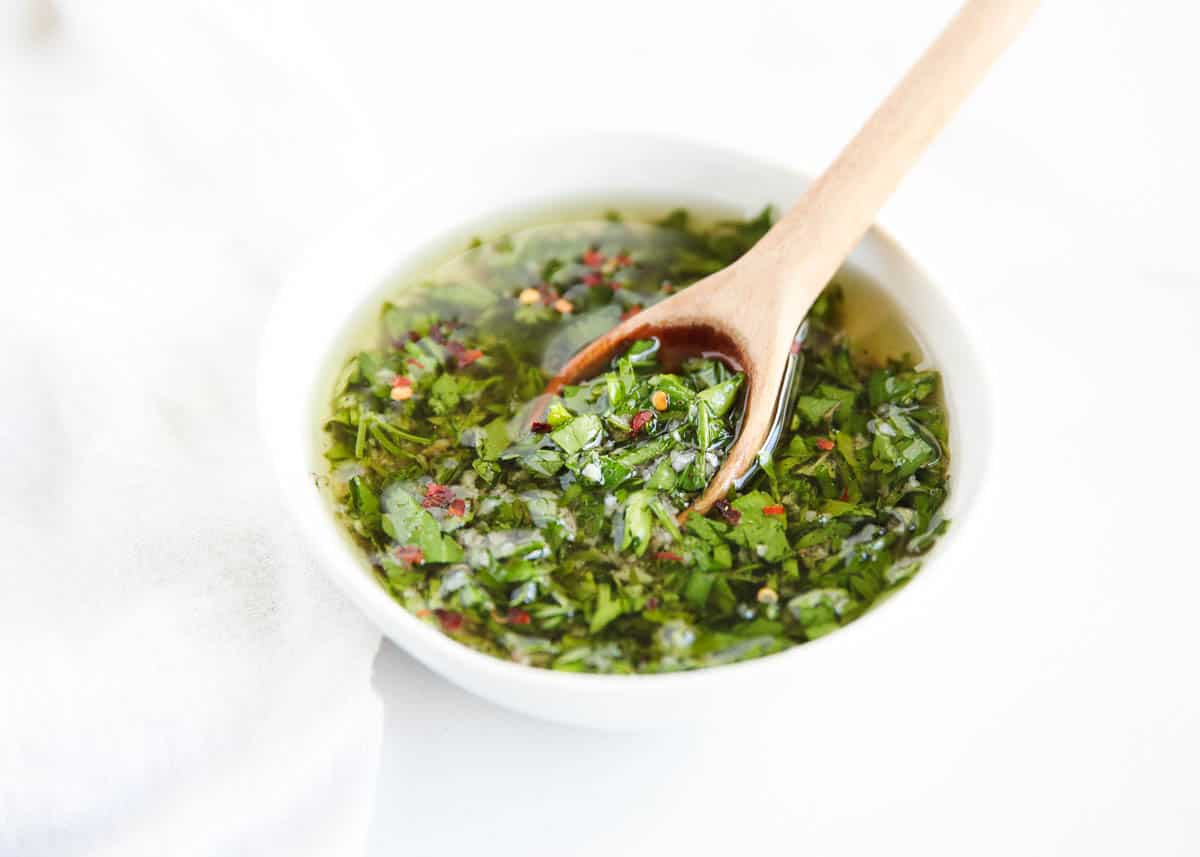 Homemade chimichurri in white bowl with wooden spoon.
