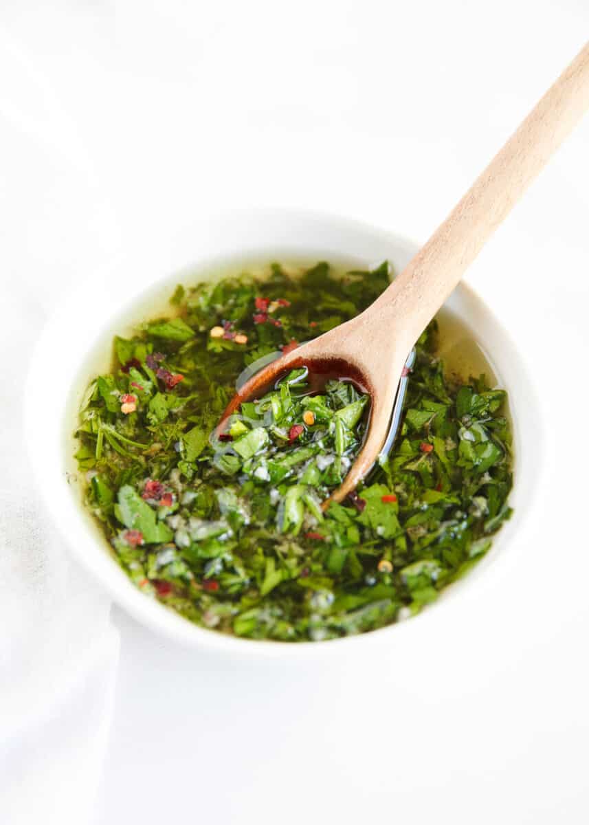 Chimichurri in white bowl with wooden spoon.