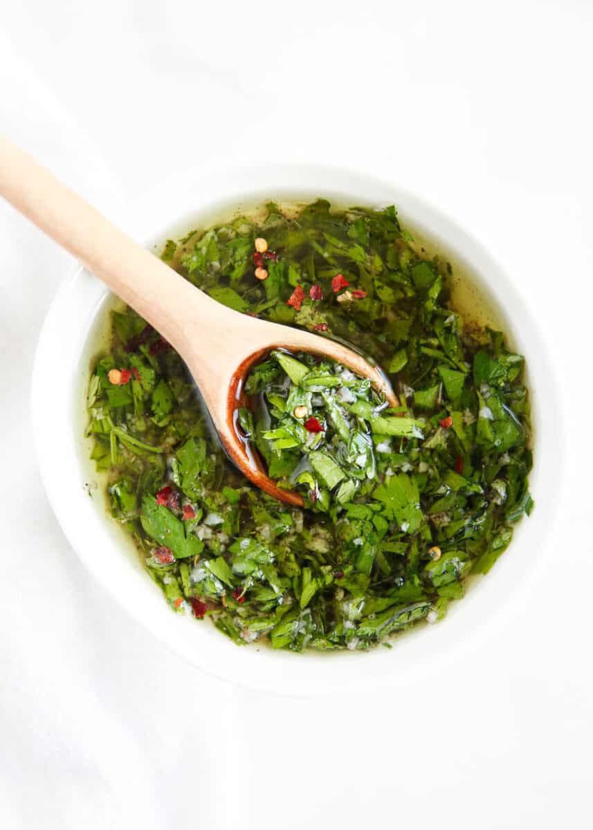 Homemade chimichurri in white bowl with spoon.