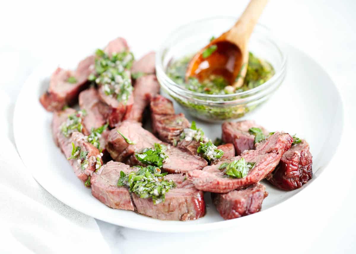 Sliced chimichurri steak on white plate. 