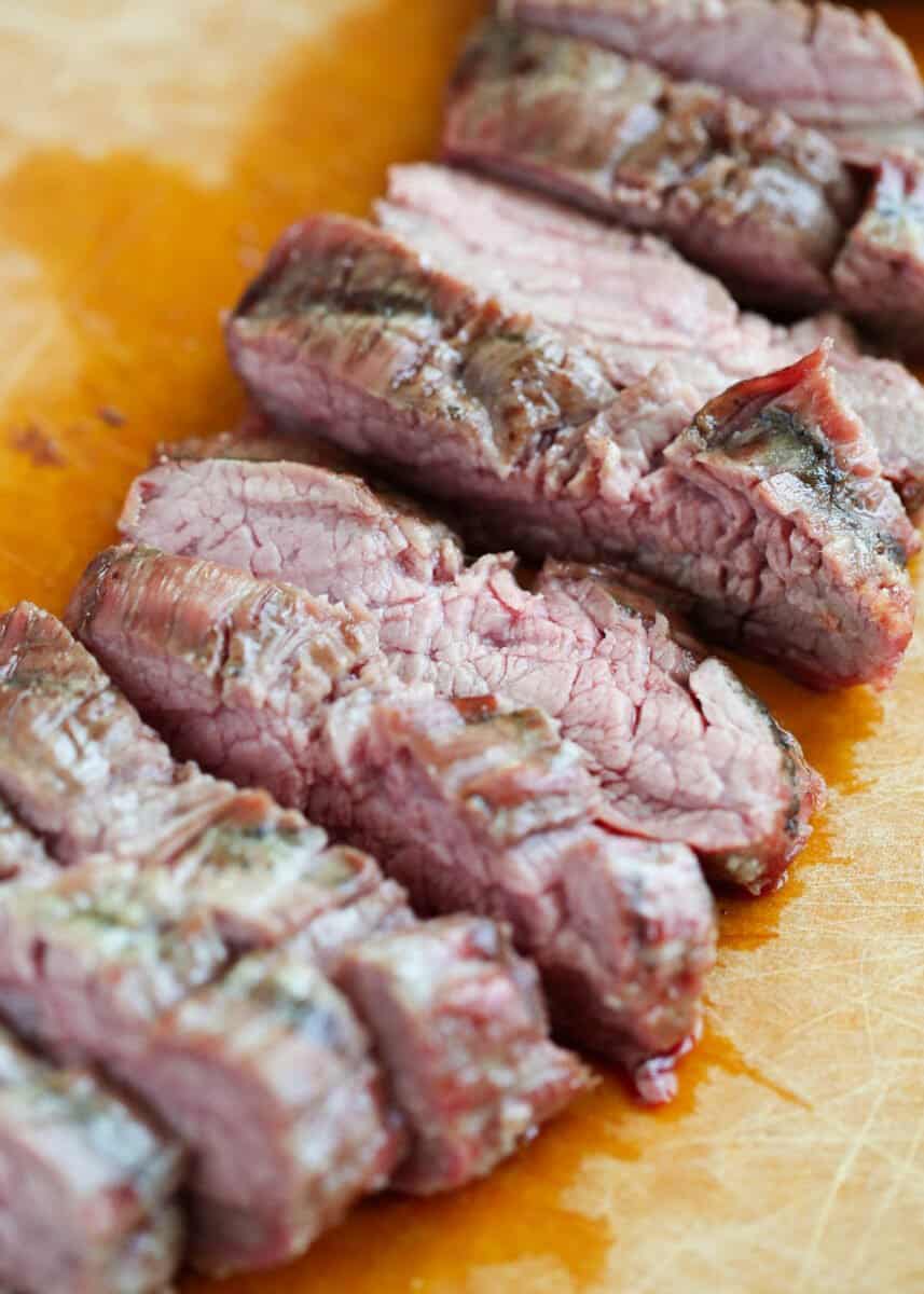Sliced flank steak on a wooden cutting board.