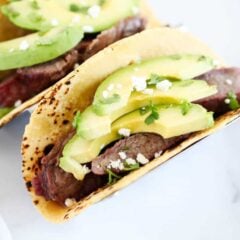 Flank steak tacos in a tortilla with sliced avocados and cilantro.