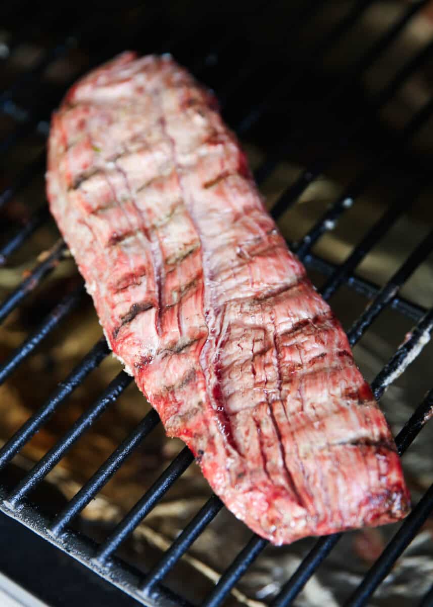 Flank steak cooking on a grill.