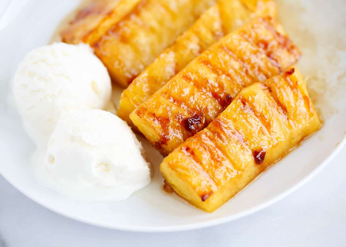 Grilled pineapple and vanilla ice cream on white plate.