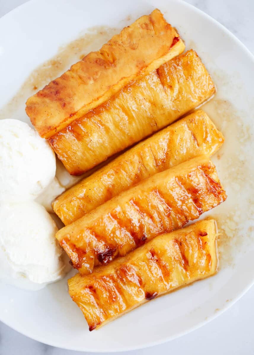 Grilled pineapple slices and vanilla ice cream on white plate.