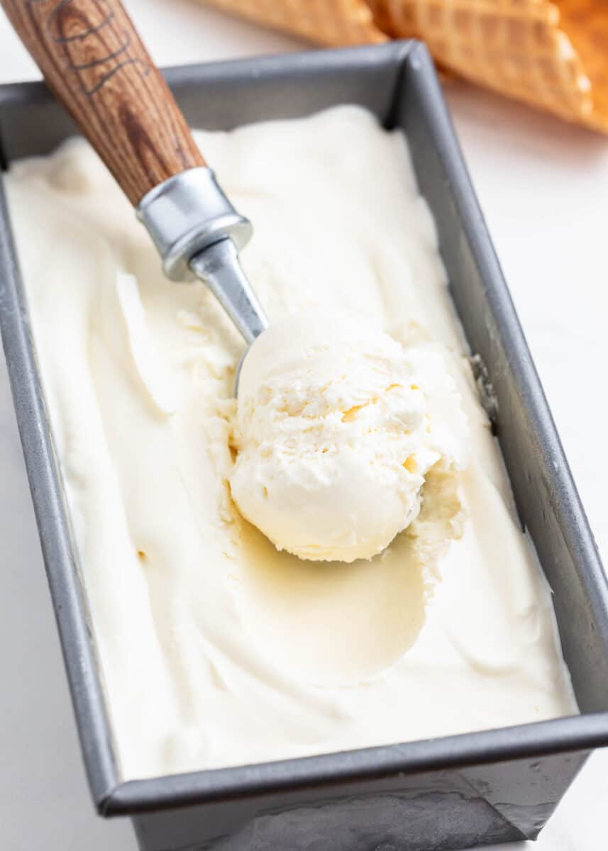 Scooping vanilla ice cream from container.