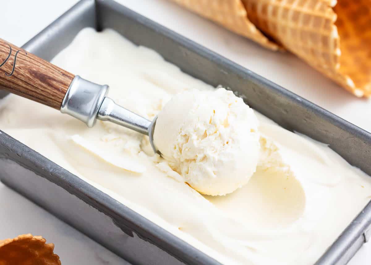 Scooping vanilla ice cream from metal container.