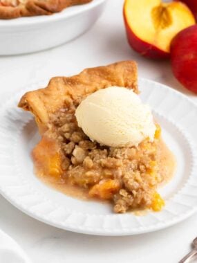 Slice of peach crumble pie with ice cream on top.