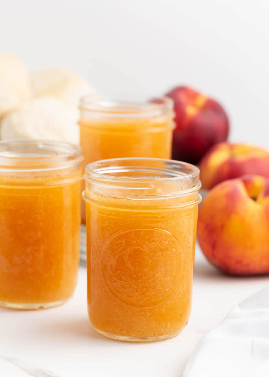 Peach jam in glass mason jars on counter.