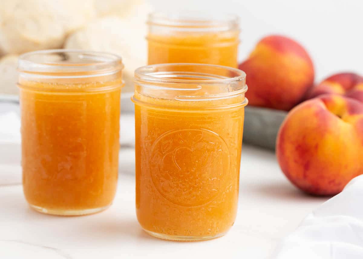 Peach jam in glass jars on counter.