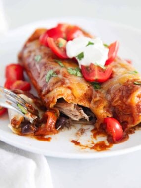 Pork enchiladas on white plate with bite taken.