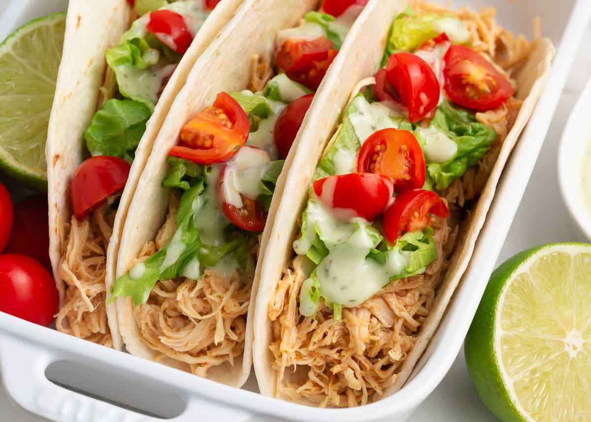 Ranch chicken tacos with lettuce and tomatoes in white dish. .