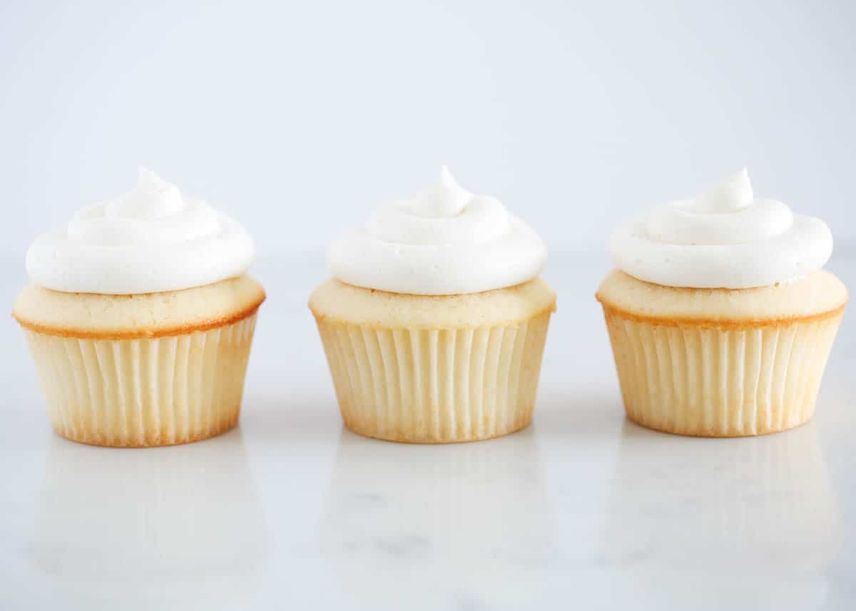 Vanilla cupcakes with frosting on counter.