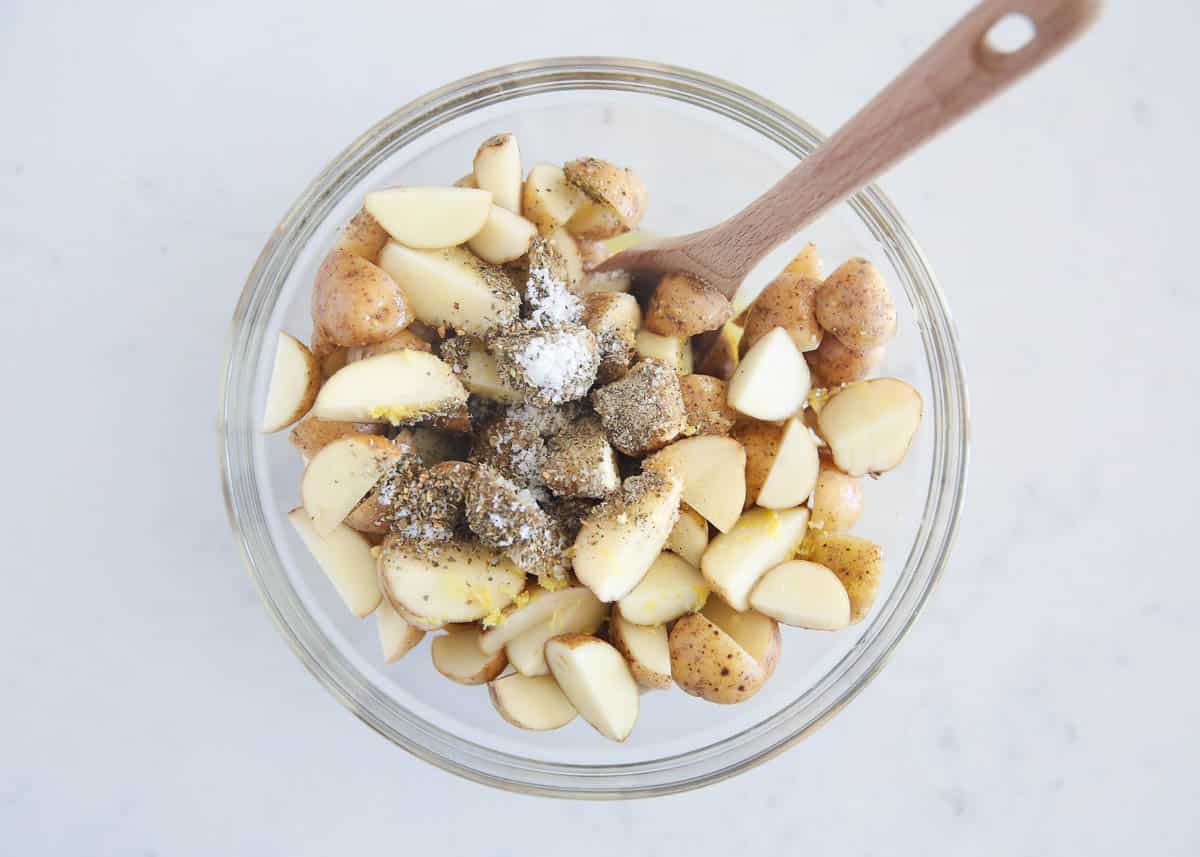 Potatoes cut into quarter in a glass bowl with seasonings.