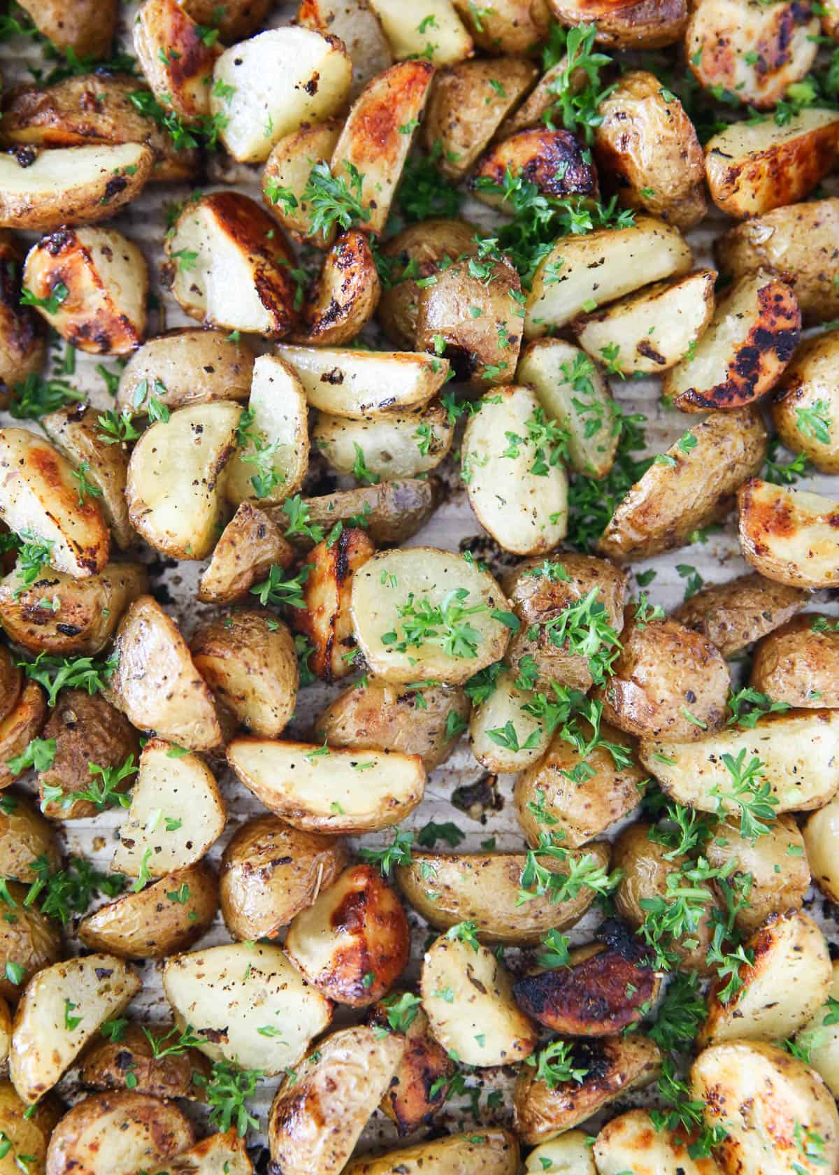 Roasted Greek potatoes on a baking sheet topped with fresh herbs.