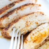 Sliced baked chicken breast on a white plate with fork.