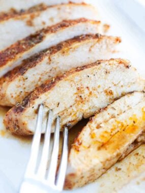 Sliced oven baked chicken breast served on a white plate showing juicy tender interior.