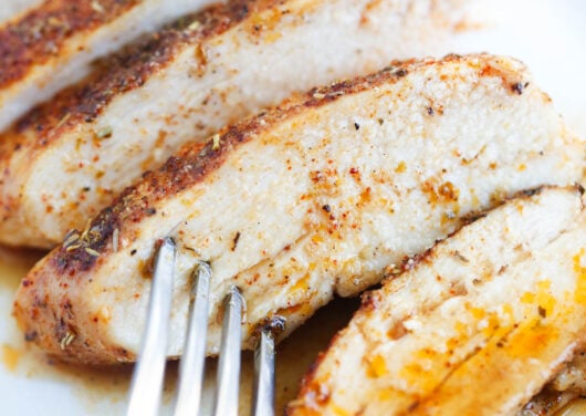 Sliced baked chicken breast on a white plate with fork.