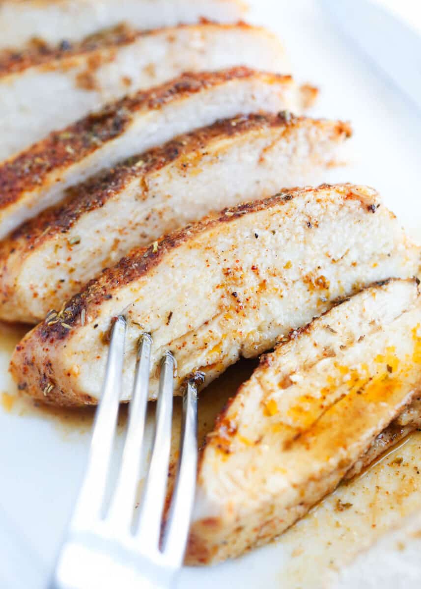 Sliced baked chicken breast on a white plate with fork.
