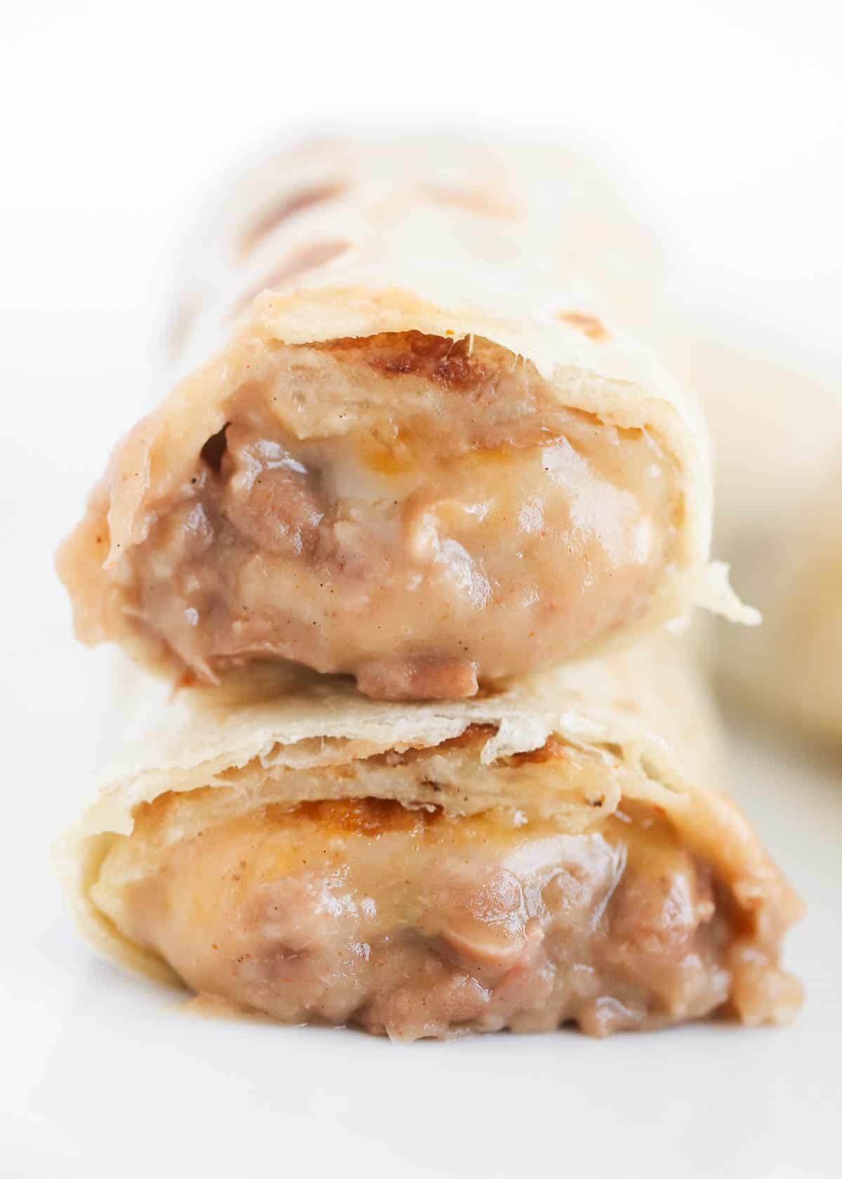 Bean and cheese burritos stacked on top of a white plate.