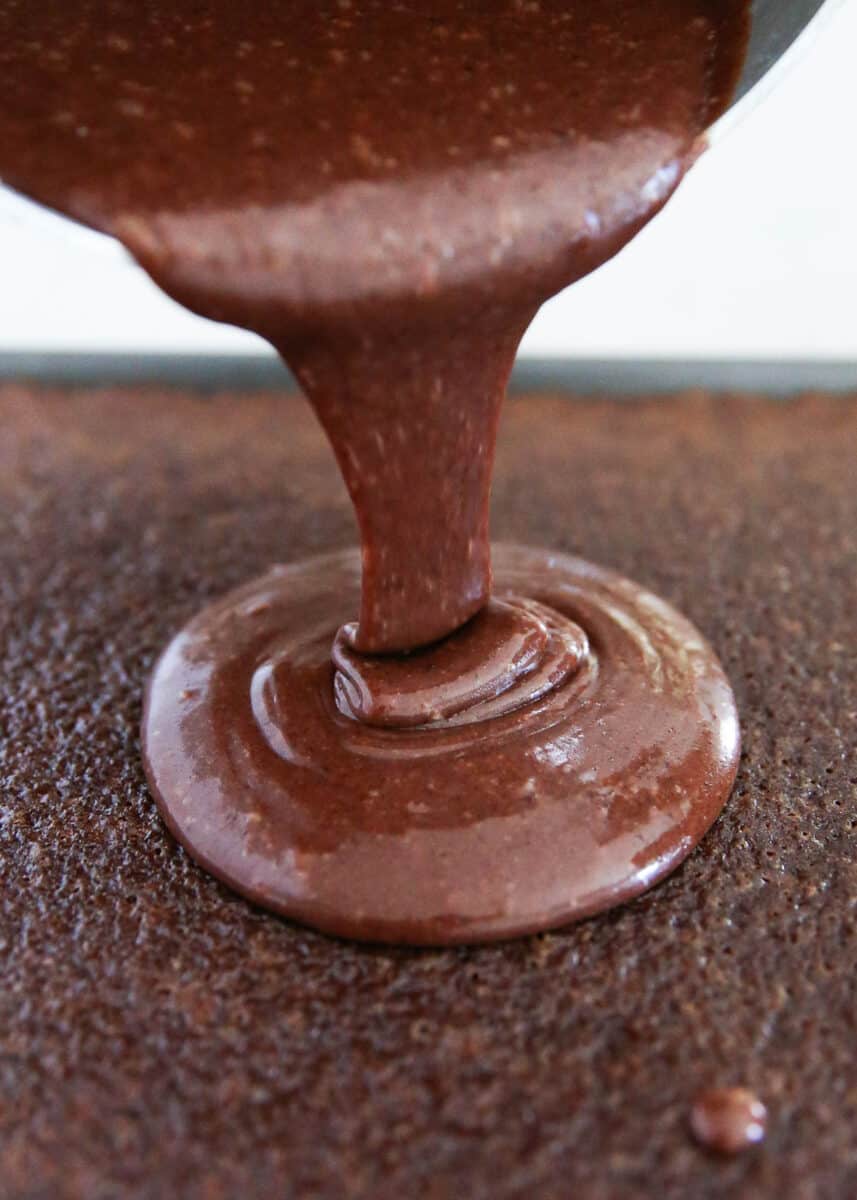 Cooked chocolate icing being poured on top of cake.