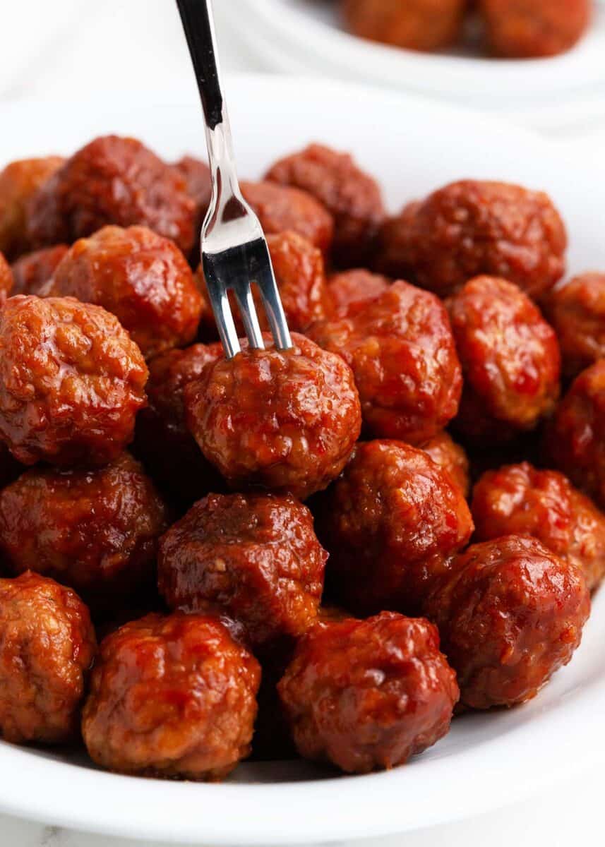 Grape jelly chili sauce meatballs on white plate with fork. 