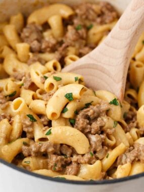 Close-up of creamy homemade hamburger helper being stirred with a wooden spoon.