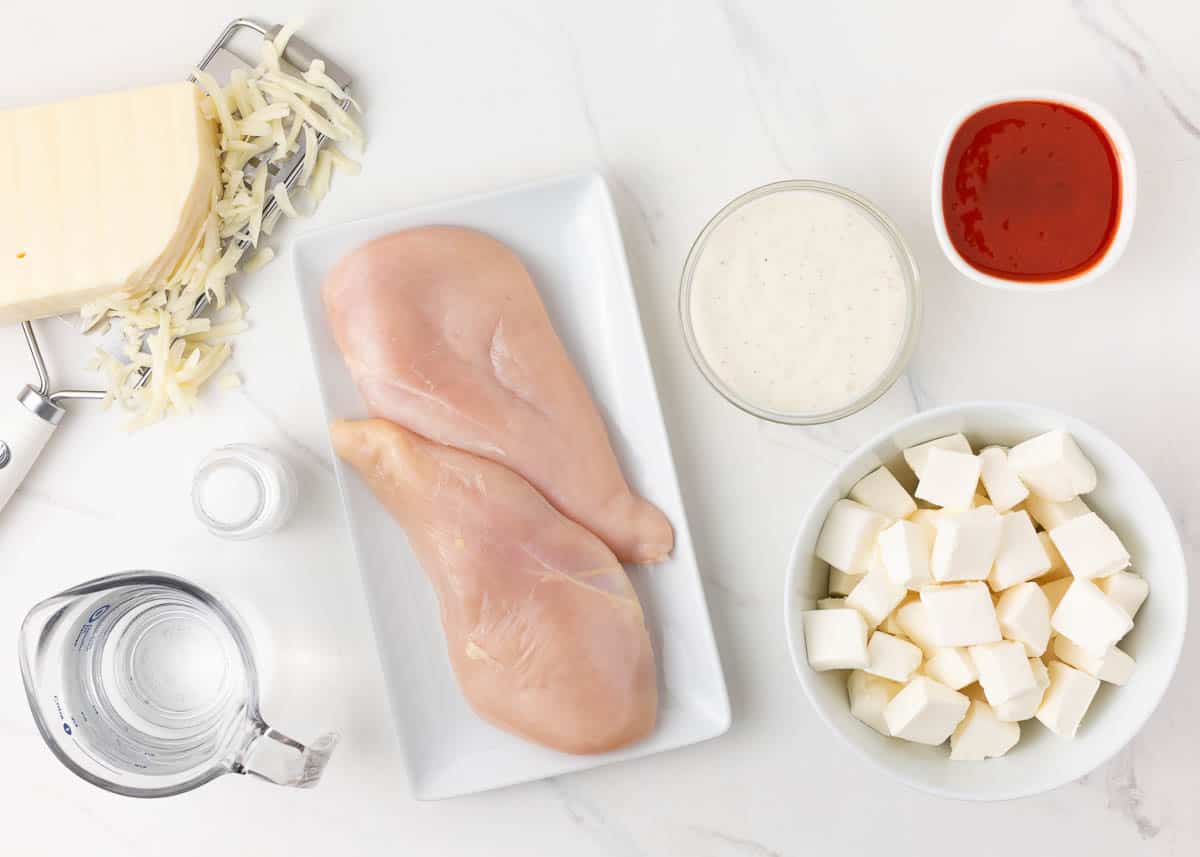 Buffalo chicken dip ingredients on marble counter.