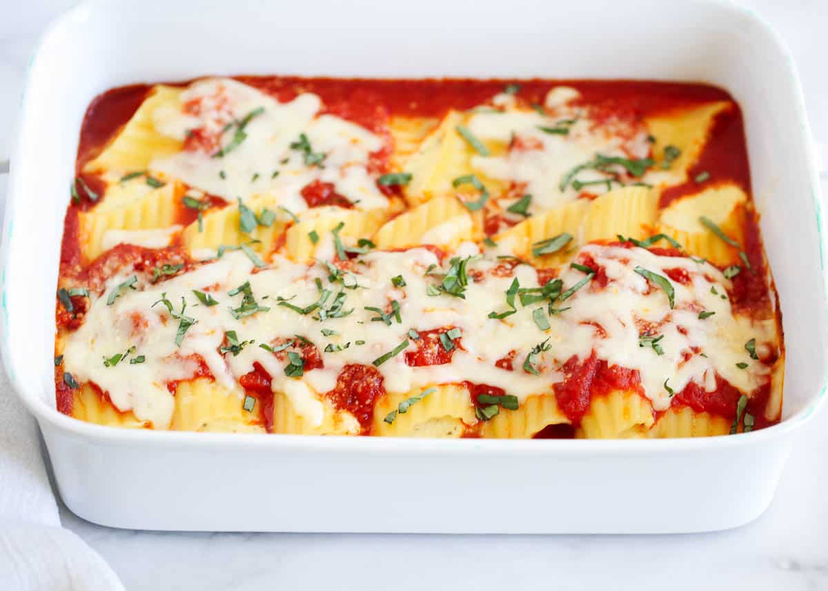 This three cheese manicotti is made with manicotti noodles stuffed with mozzarella cheese, ricotta and Parmesan, covered with marinara, baked then topped with fresh basil! Baked cheese manicotti in a baking dish.