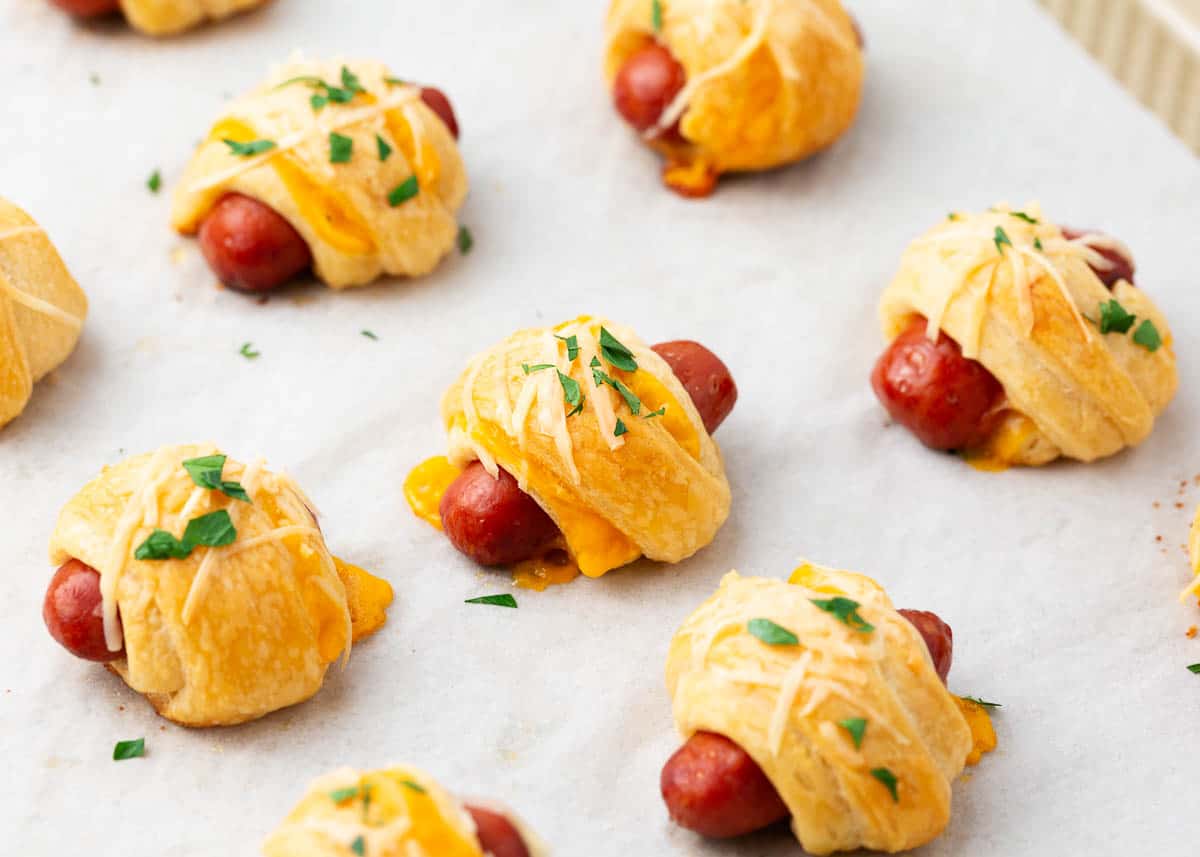 Pigs in a blanket with cheese on top on baking sheet.