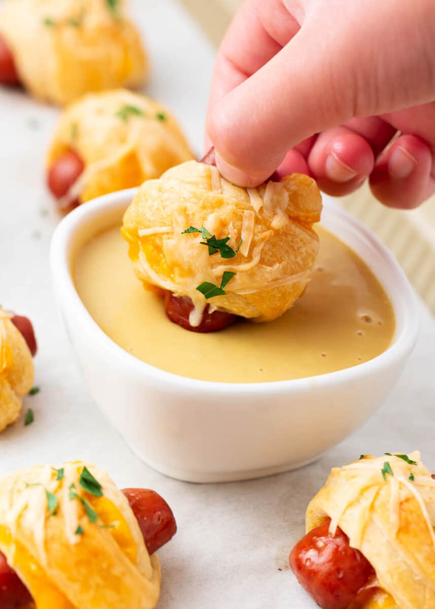 Dipping pigs in a blanket in cheese dip.