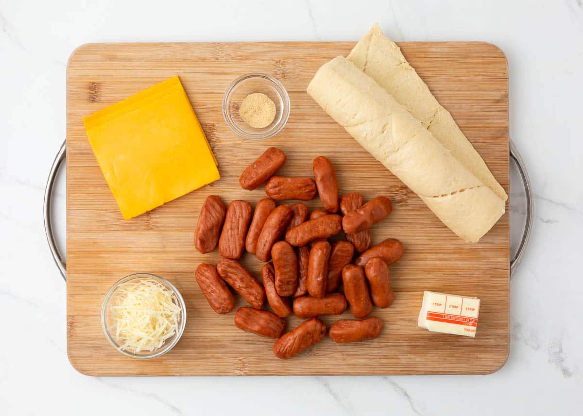 Pigs in a blanket with cheese ingredients on wooden board.