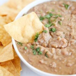Refried beans in a white bowl with a chip dipped in.