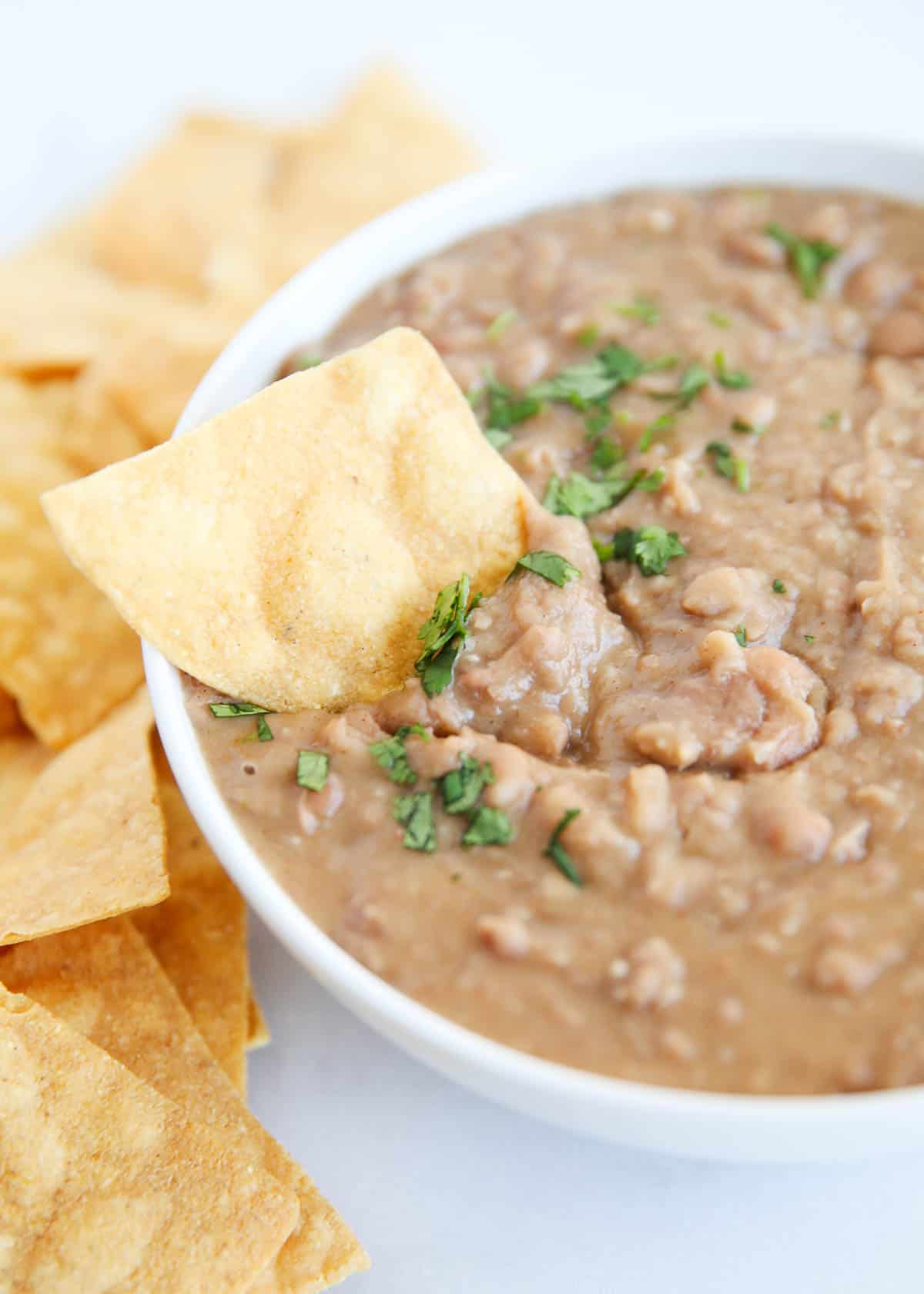 Refried beans in a white bowl with a chip dipped in.