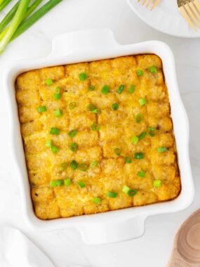 Tater tot breakfast casserole in a white baking dish with green onions.