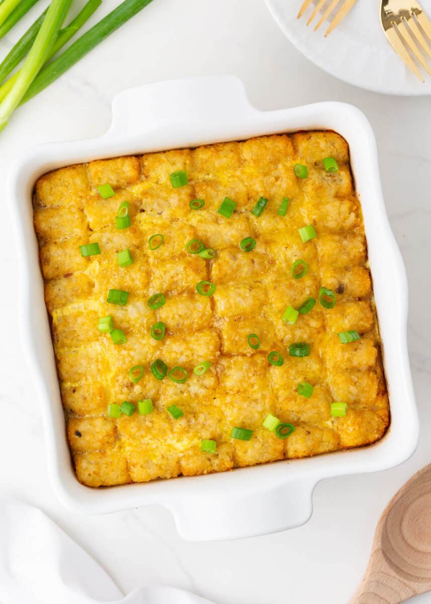 Tater tot breakfast casserole in a white baking dish with green onions.