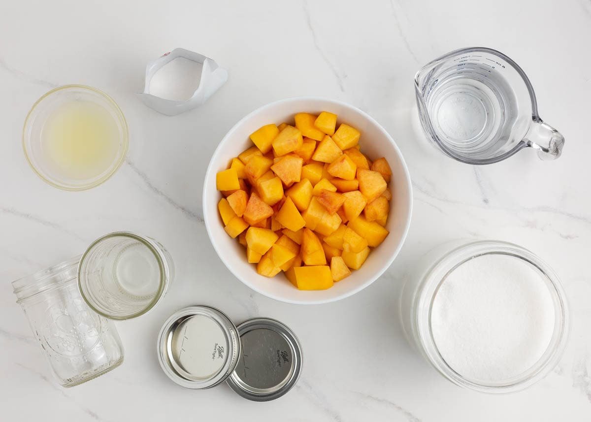 Ingredients for peach freezer jam, including chopped peaches, sugar, lemon juice, pectin, and water.