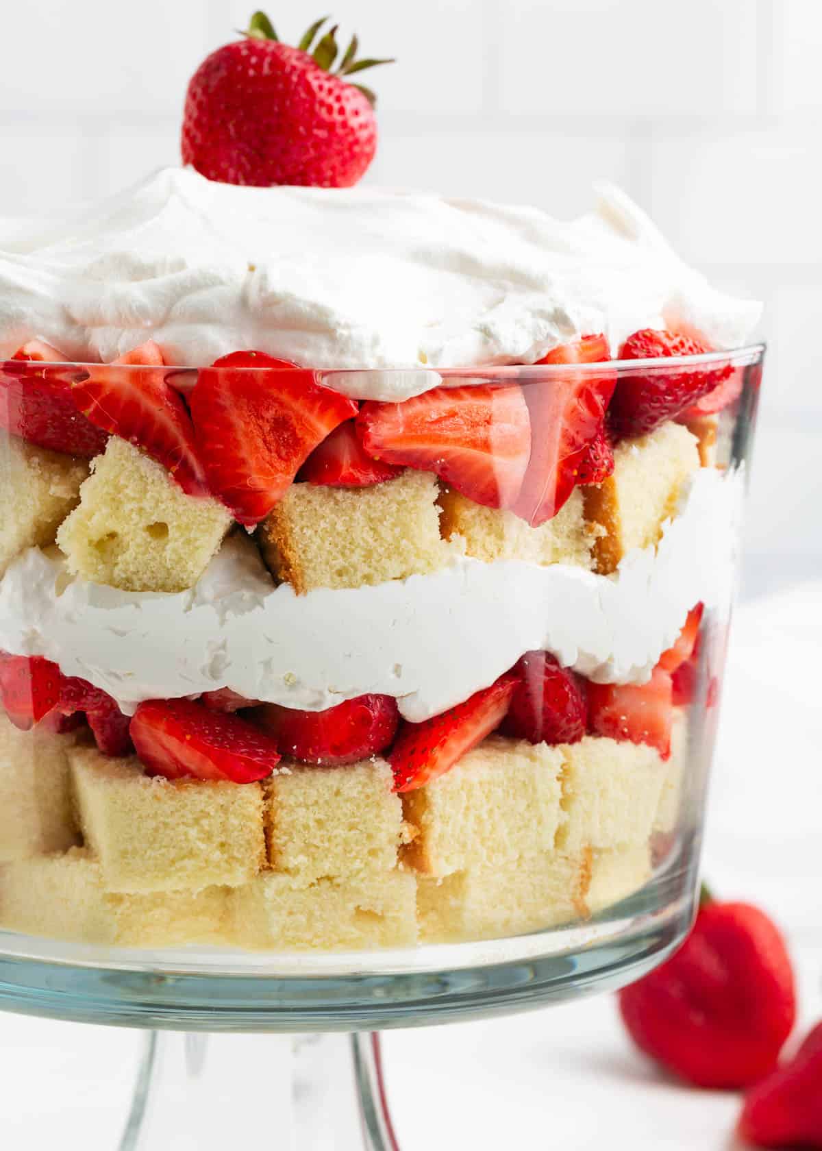 Strawberry shortcake trifle layered in a trifle dish with pound cake, cream and sliced strawberries.