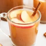 Homemade apple cider in glass cup with apples and cinnamon stick.