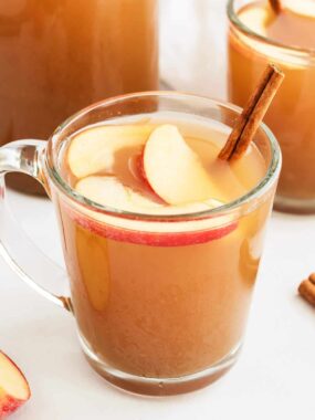 Homemade apple cider in glass cup with apples and cinnamon stick.