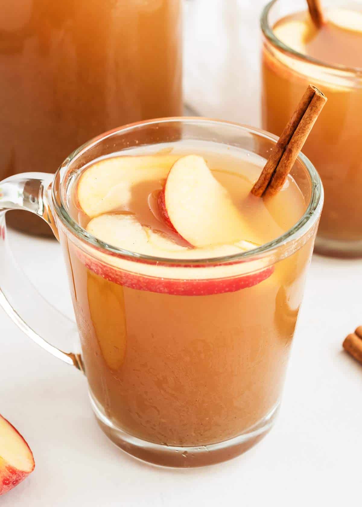 Homemade apple cider in glass cup with apples and cinnamon stick.