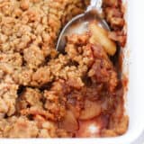 A spoon scooping out apple crumble from pan.