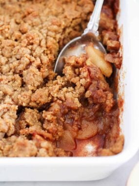 A spoon scooping out apple crumble from pan.