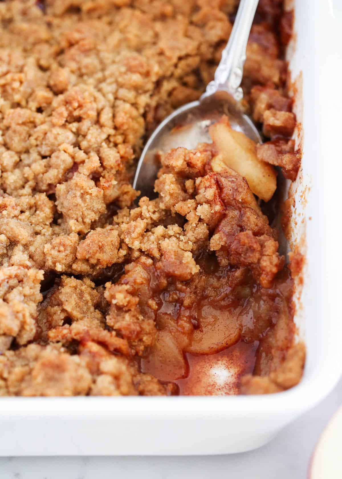 A spoon scooping out apple crumble from pan.